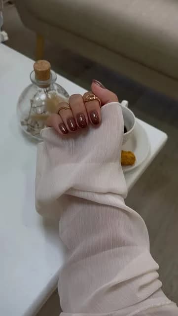 Unhas bordeaux brilhantes junto a uma chávena