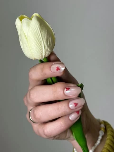 Mão a segurar uma tulipa com unhas nude e corações vermelhos